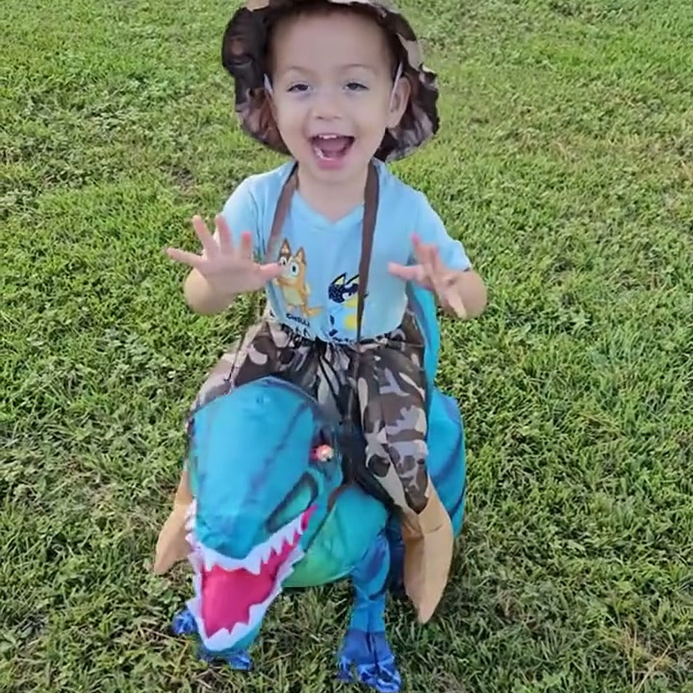 Smiling child riding a blue Raptie dinosaur costume on the lawn